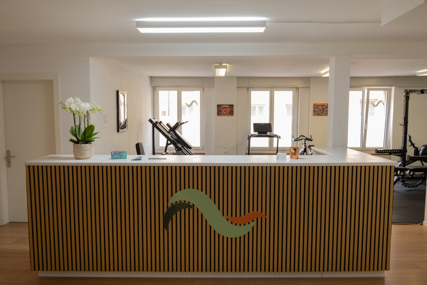 Le comptoir d’accueil en lattes de bois, marqué du symbole MOVEO, devant la salle d’entraînement